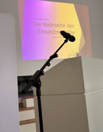 Veteranenwochenende 2024 mit dem 8.Tag der EinsatzVeteranen 4 Mikrofon am Pult mit Wasserglas vor Leinwand, Präsentation "Die Kehrseite der Einsatzmedaille", Bund Deutscher Veteranen.