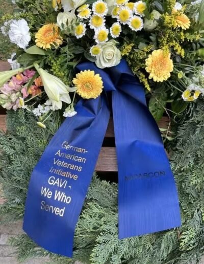 Veteranenwochenende 2024 mit dem 8.Tag der EinsatzVeteranen 74 Blumengesteck mit gelben und weißen Blumen, Grün und blauem Band zum Gedenken deutscher Veteranen, goldene Inschrift.