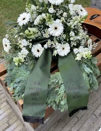 Veteranenwochenende 2024 mit dem 8.Tag der EinsatzVeteranen 72 Trauerkranz mit weißen Blumen und Schleifen, Aufschrift "Wir werden euch nie vergessen", Gitarre daneben, Bund Deutscher Veteranen.