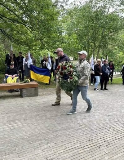 Veteranenwochenende 2024 mit dem 8.Tag der EinsatzVeteranen 37 Zwei Männer tragen bei einer Gedenkfeier des Bund Deutscher Veteranen im Freien einen Kranz, Fahnen und Teilnehmer im Hintergrund.