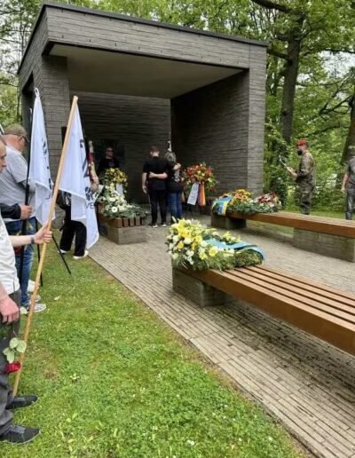Veteranenwochenende 2024 mit dem 8.Tag der EinsatzVeteranen 40 Trauerfeier am modernen Gedenkort des Bund Deutscher Veteranen, Menschen um Sarg mit blau-gelbem Tuch und Blumenschmuck.