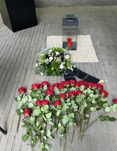 Veteranenwochenende 2024 mit dem 8.Tag der EinsatzVeteranen 78 Rote Rosen und weiße Blumen liegen vor einer brennenden roten Kerze in der Laterne auf Kies, Gedenken Bund Deutscher Veteranen.