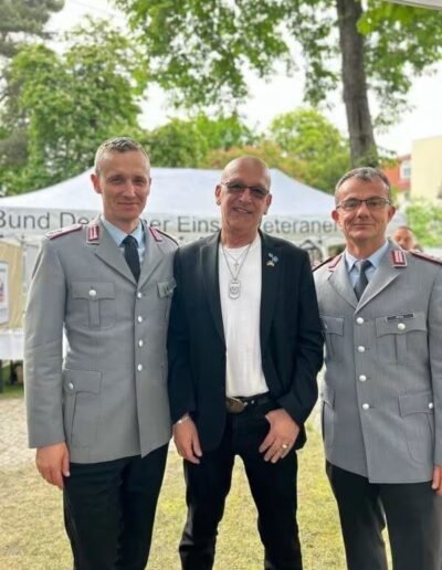 Veteranenwochenende 2024 mit dem 8.Tag der EinsatzVeteranen 10 Drei Männer beim Bund Deutscher Veteranen: Zwei in Uniform, einer in Zivil. Im Hintergrund ein Zelt und grüne Natur.