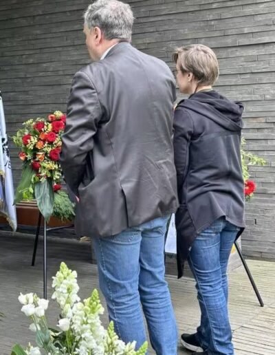 Veteranenwochenende 2024 mit dem 8.Tag der EinsatzVeteranen 59 Zwei Personen stehen eng beieinander vor Blumen und Sarg bei einer Trauerfeier, Thema Bund Deutscher Veteranen.