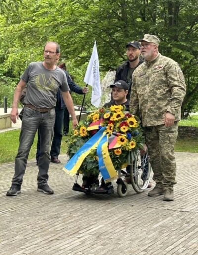 Veteranenwochenende 2024 mit dem 8.Tag der EinsatzVeteranen 34 Mann im Rollstuhl mit Kranz, begleitet von drei Männern, darunter ein Soldat, beim Gedenken des Bund Deutscher Veteranen draußen.