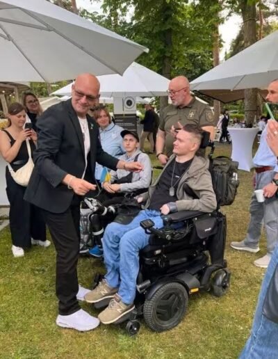 Veteranenwochenende 2024 mit dem 8.Tag der EinsatzVeteranen 13 Menschen im Freien beim Bund Deutscher Veteranen, zwei Rollstuhlfahrer lächeln, andere stehen dazu und fotografieren.