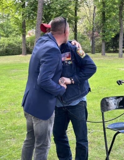 Veteranenwochenende 2024 mit dem 8.Tag der EinsatzVeteranen 24 Zwei Männer, einer im Blazer, einer mit bedeckter Weste vom Bund Deutscher Veteranen, begrüßen sich herzlich im Park.